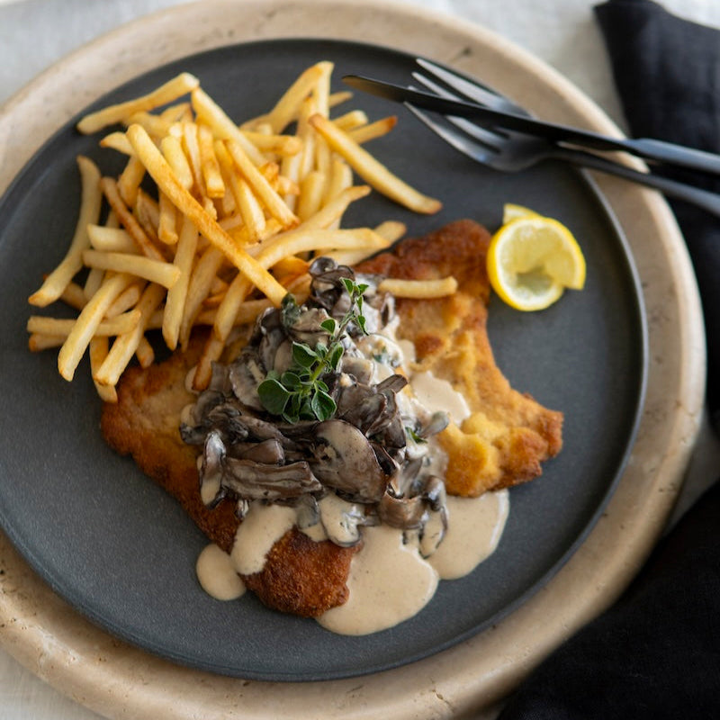 Plated dish with Schnitzel, fries, and a side of mushroom sauce on a gray plate.