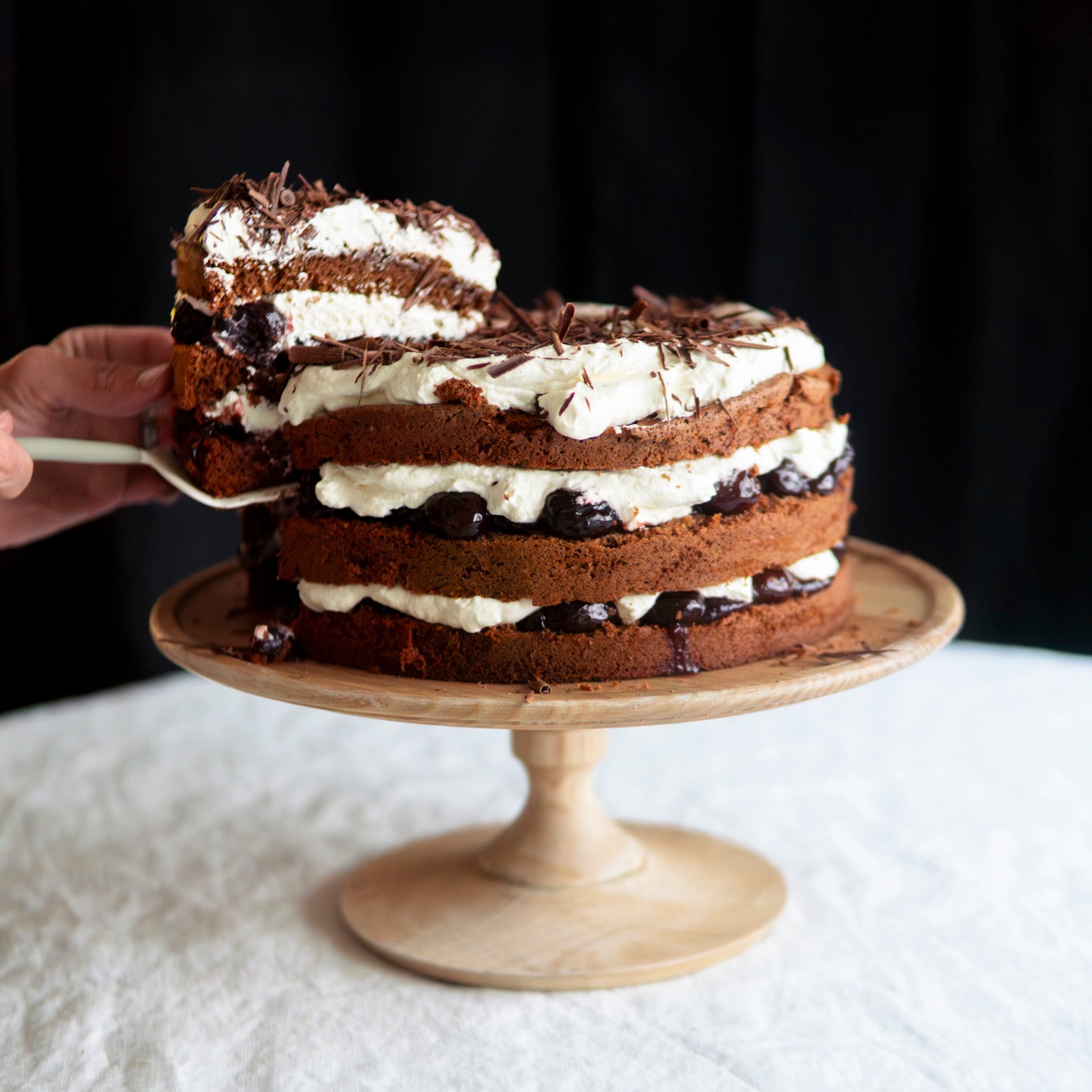 Black Forest cake on a wooden cake stand against a black background